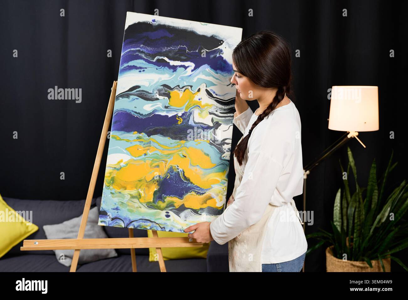 Jeune femme exprime son talent artistique à la maison tout en mettant en valeur une peinture vibrante. Banque D'Images