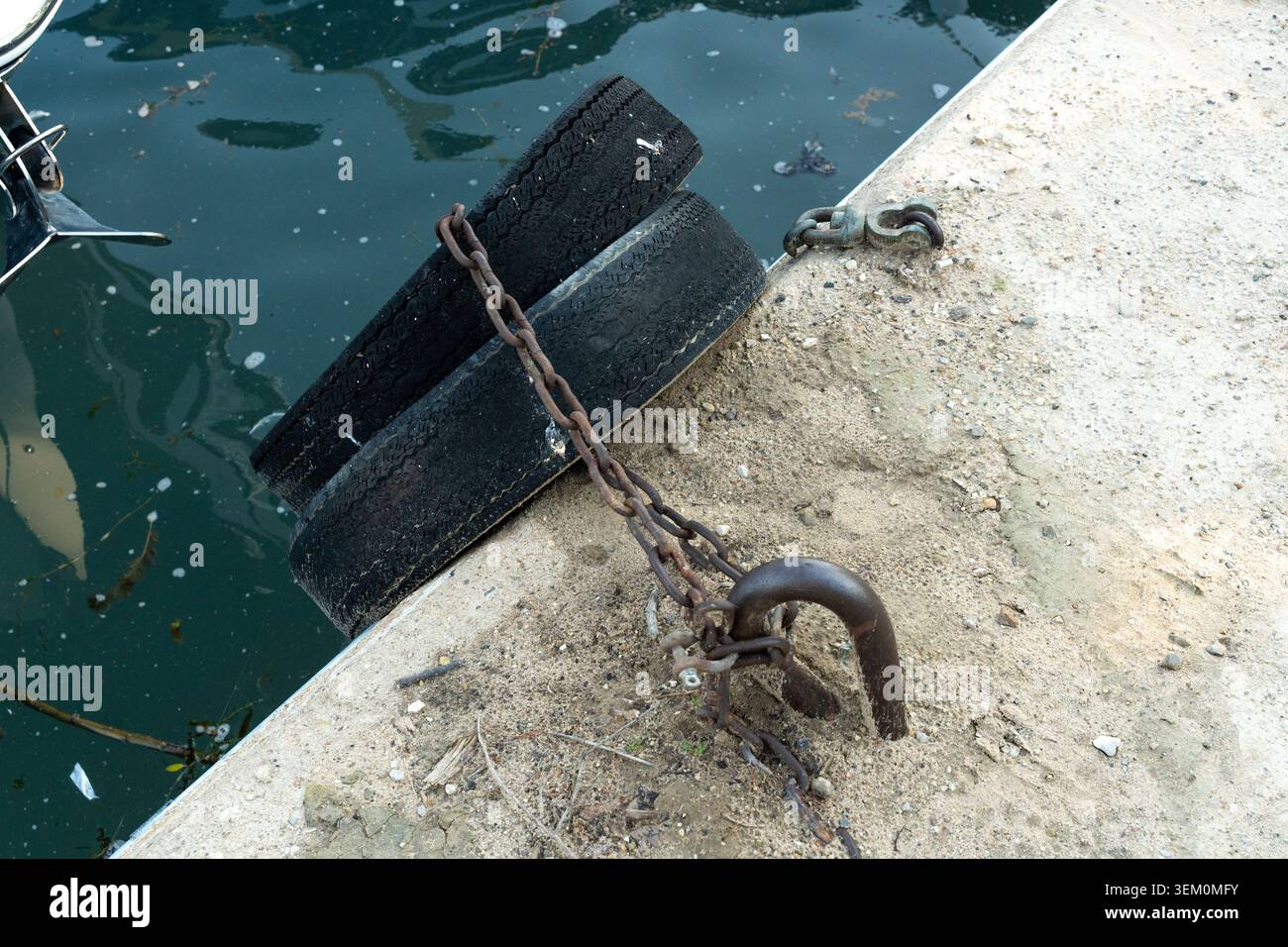 Chaîne en métal vieilli fixant les anciens pare-chocs à un quai en béton, avec matériel d'amarrage rouillé dans un cadre de front de mer en bon état Banque D'Images