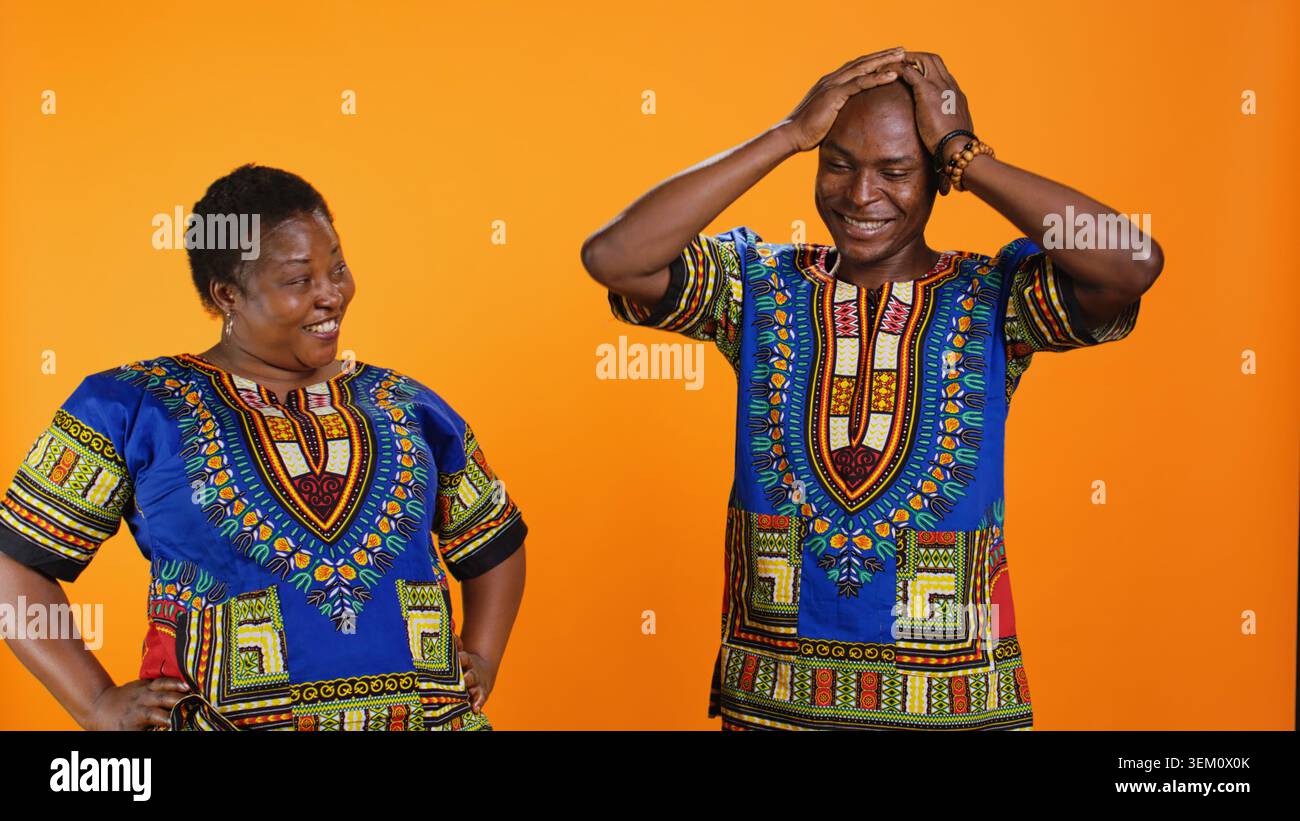 Joyeux homme et femme riant ensemble en studio, s'amusant avec des blagues stupides sur fond orange. Les Afro-américains apprécient des moments drôles avec rire, couple amusé. Banque D'Images