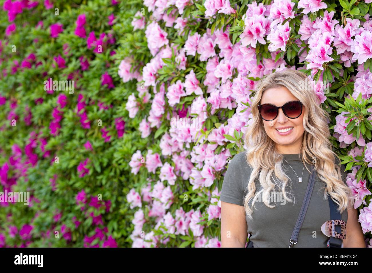 Femme blonde se tient devant un mur de fleurs roses, portrait Banque D'Images