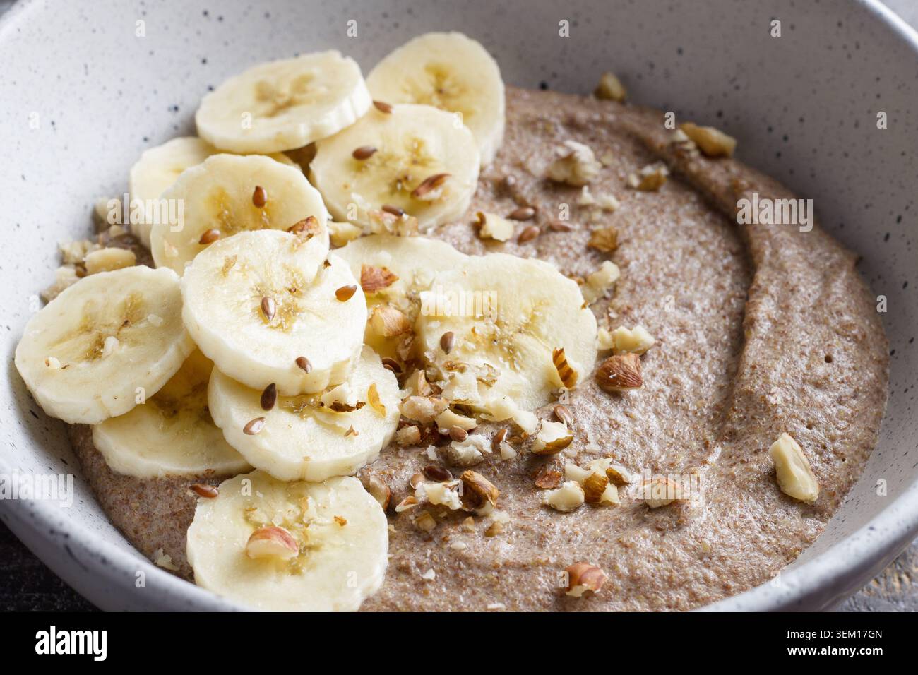 Bouillie de lin saine garnie de tranches de banane, de noix hachées et de graines dans un bol en céramique. Petit déjeuner nutritif avec des ingrédients naturels, gros plan Banque D'Images