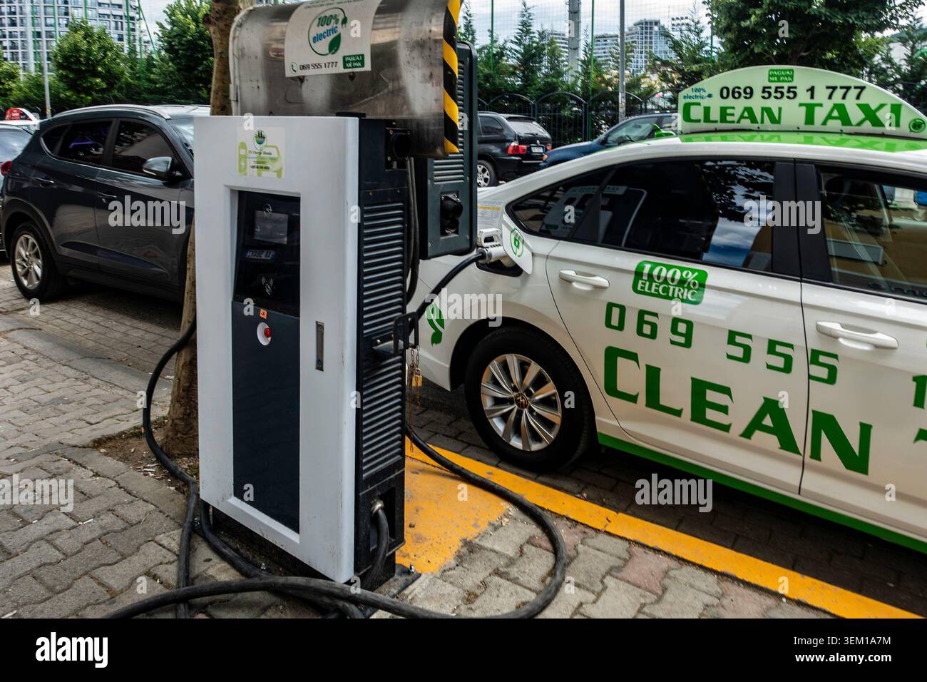 Un taxi propre électrique blanc connecté à une station de recharge publique EV sur une place de parking de rue pavée à Tirana, en Albanie. Banque D'Images