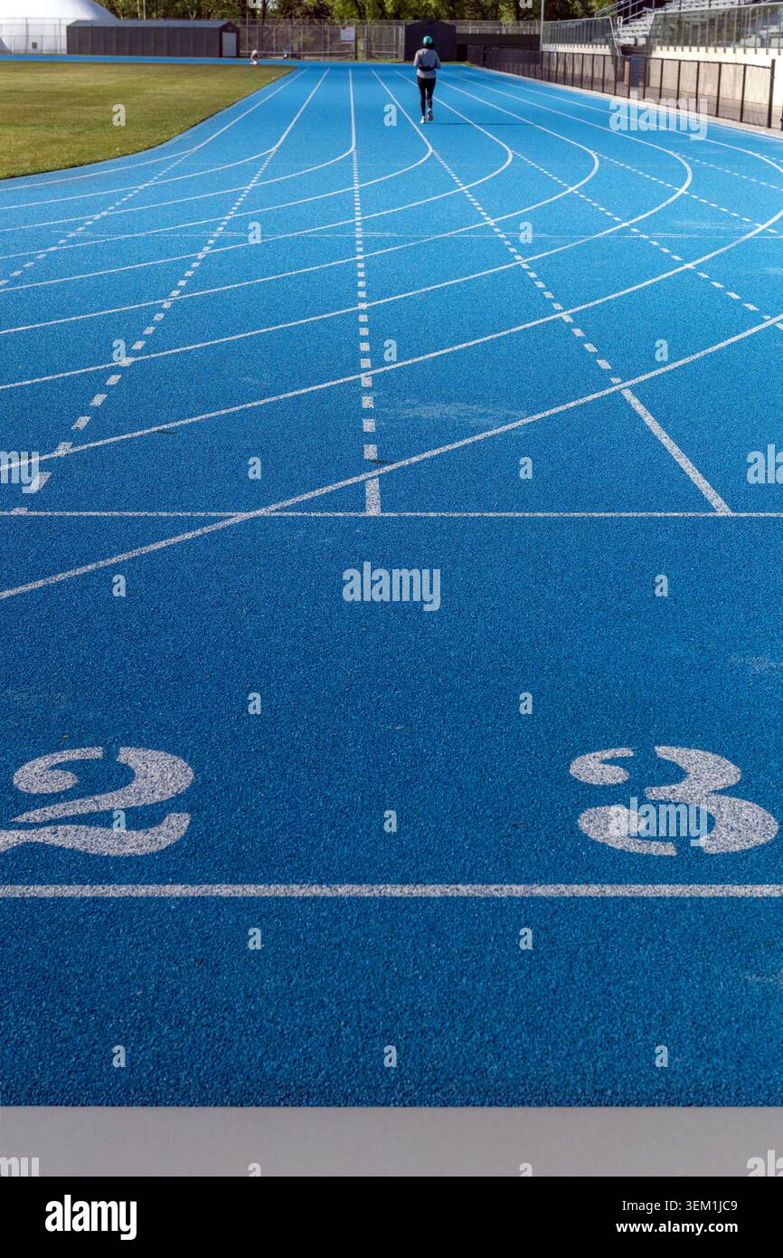 Piste de course bleue avec jogging fenmale et marquage des voies dans un stade d'athlétisme extérieur. Banque D'Images