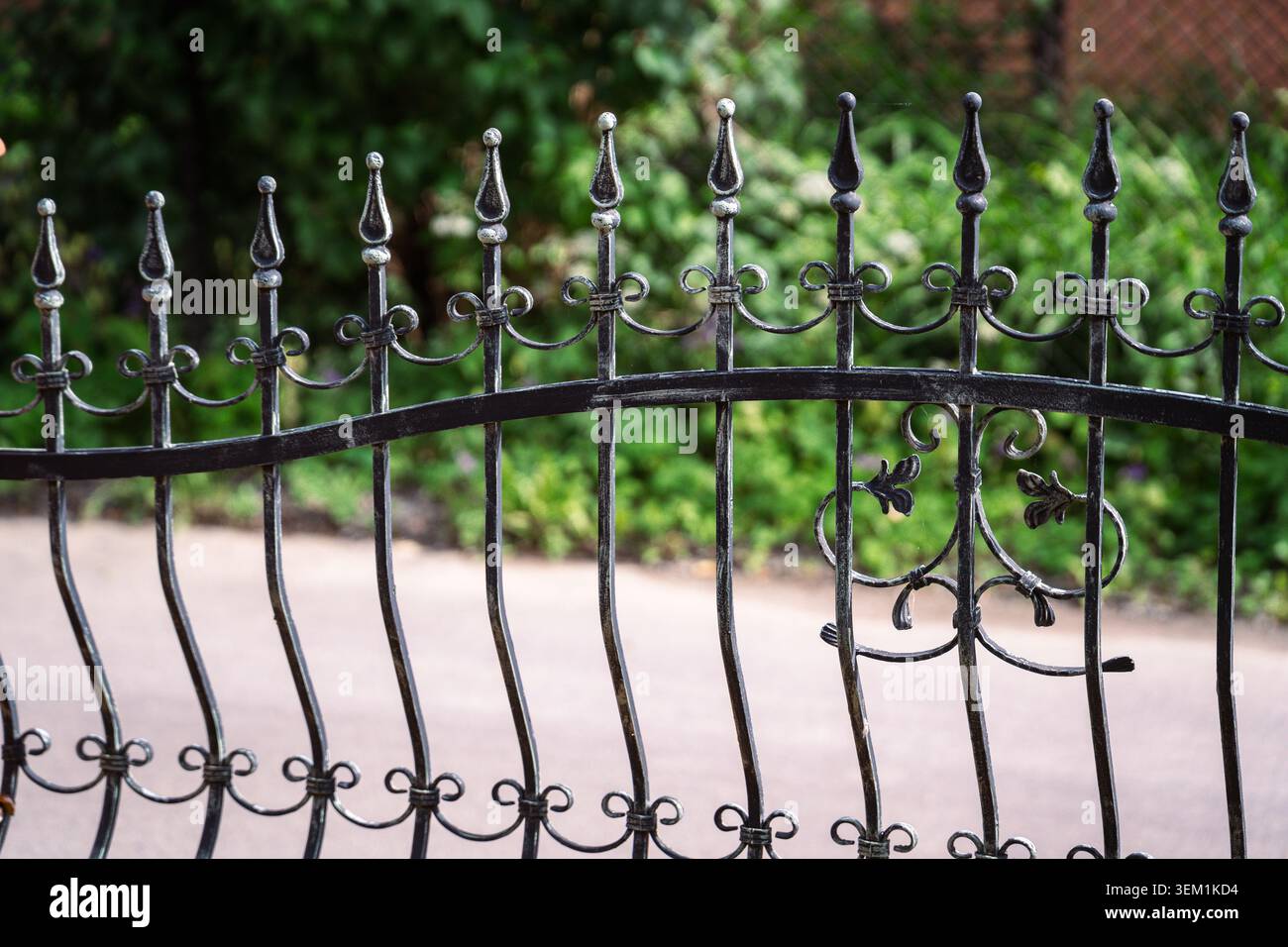 Clôture décorative en fer forgé noir avec des pointes en métal ornées devant un jardin verdoyant Banque D'Images