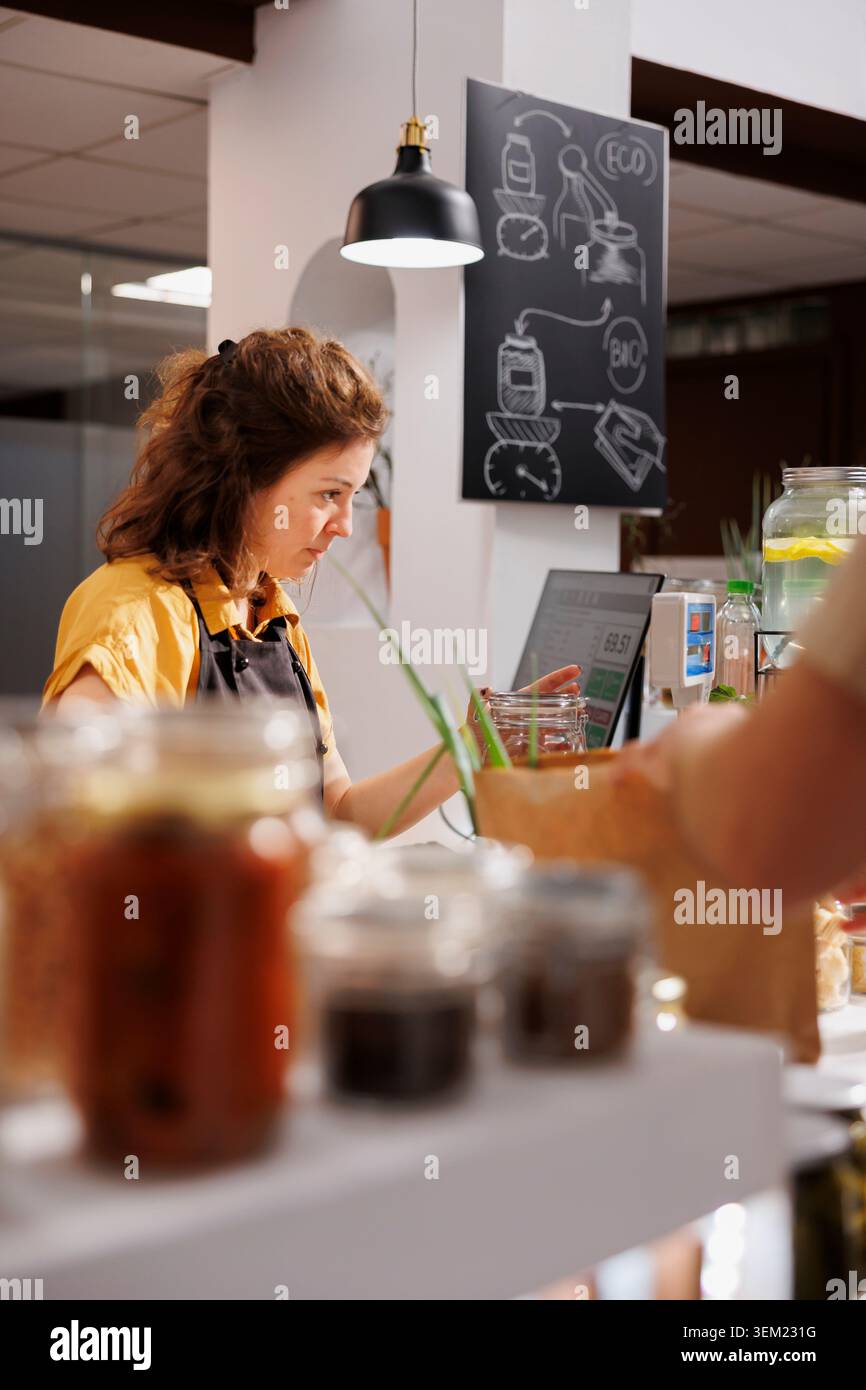 Magasin à la caisse de supermarché zéro déchet utilisant un lecteur de code-barres pour traiter les transactions client. Vendeur dans un magasin de quartier durable scannant les produits alimentaires des clients Banque D'Images