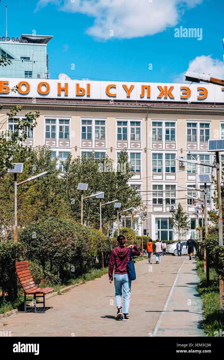 Des piétons marchent vers un bâtiment marqué "Wholesale Network" le long d'un chemin verdoyant à Oulan-Bator, en Mongolie. Banque D'Images