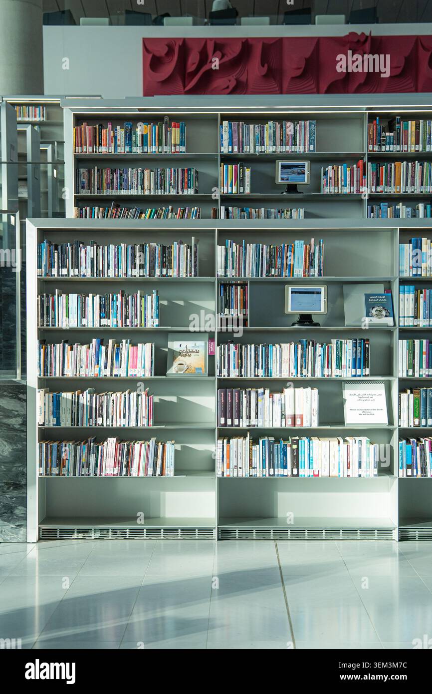 Rangées de livres sur de grandes étagères dans un intérieur de bibliothèque moderne avec des postes informatiques et un sol vide lumineux Banque D'Images