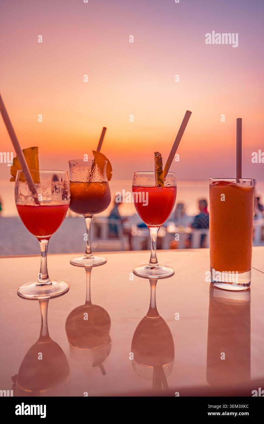Cocktails de plage dans des verres sur le bar avec coucher de soleil tropical sur l'océan et des gens en arrière-plan. Resort de vacances d'été. Paradis de voyage de vacances de plage cocktail Banque D'Images