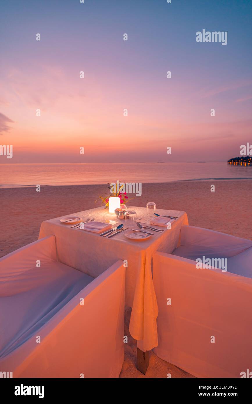 Table intime pour un dîner aux chandelles pour deux sur une plage tropicale lors d'un coucher de soleil romantique. Ciel rose au crépuscule sur l'océan. Voyage de luxe pour lune de miel et escapade Banque D'Images