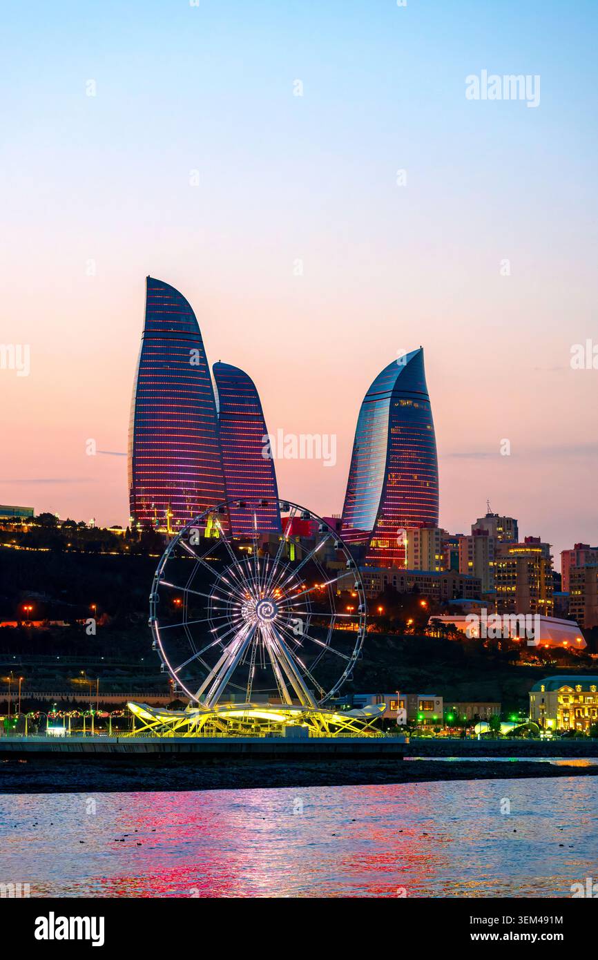 La grande roue Baku Eye s'illumine au crépuscule sur le front de mer du boulevard avec des Flame Towers rouges à l'arrière. Bakou, Azerbaïdjan. Banque D'Images