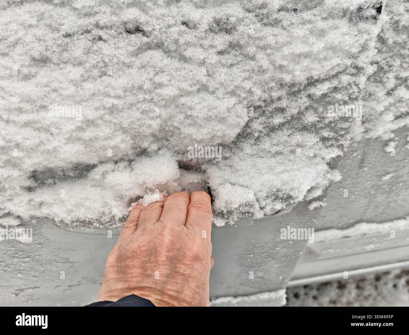 Une personne tente d'ouvrir une serrure de porte de voiture recouverte de neige et de glace, soulignant les problèmes de voiture pendant les conditions météorologiques hivernales. Banque D'Images