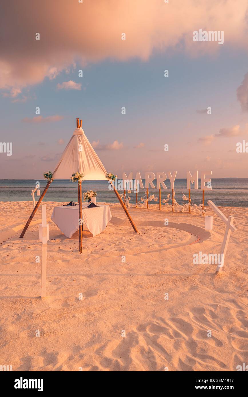 Proposition de mariage sur une plage de sable blanc, teepee avec table à manger et panneau de lettres, décoration romantique de fiançailles au bord de la mer en journée Banque D'Images