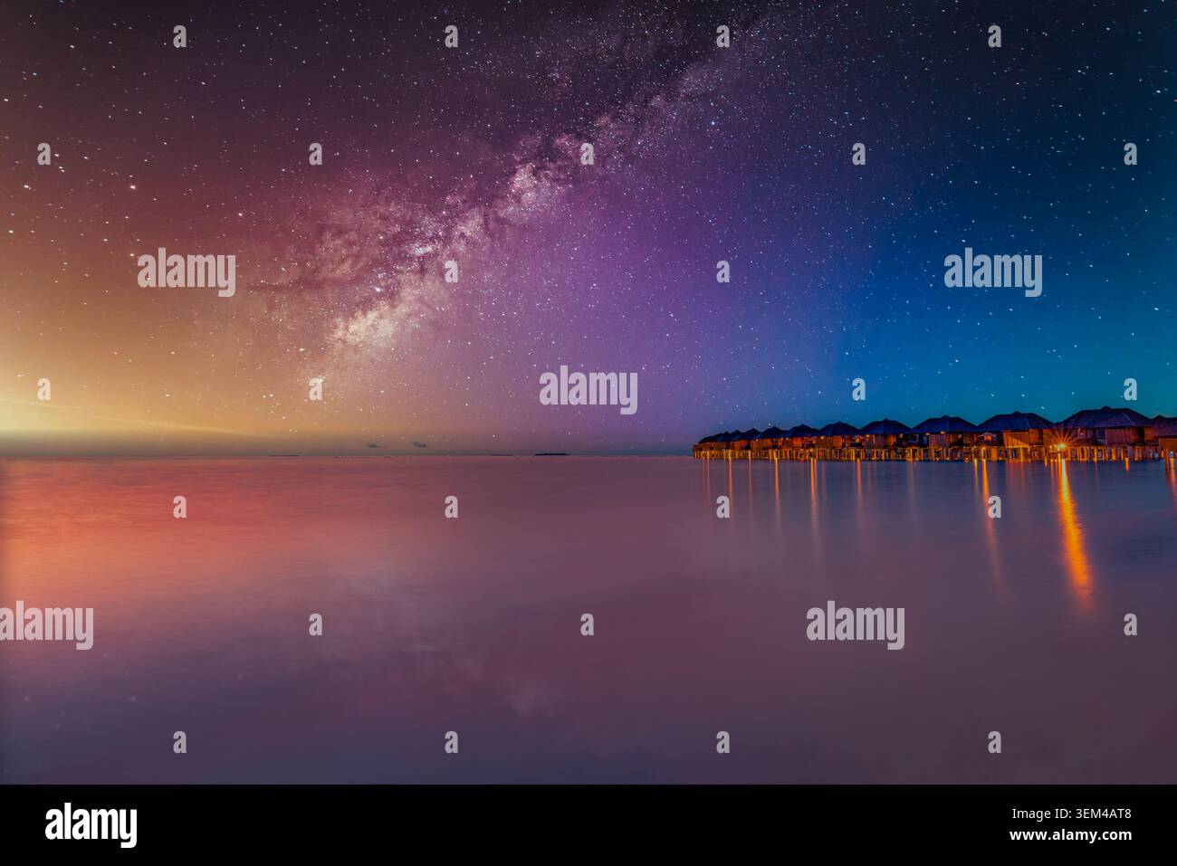 Galaxie de la Voie lactée sur une lagune tropicale la nuit, ciel étoilé violet au-dessus des villas sur l'eau avec des lumières chaudes, paysage nocturne magique d'île pittoresque. Astronomie Banque D'Images