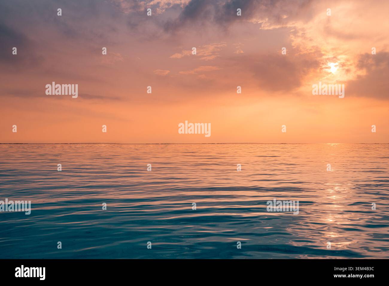 Couchant dramatique orange sur un océan calme, soleil éclatant derrière des nuages doux, paysage maritime tranquille avec reflet, ciel estival chaud à la tombée de la nuit, côte paisible Banque D'Images