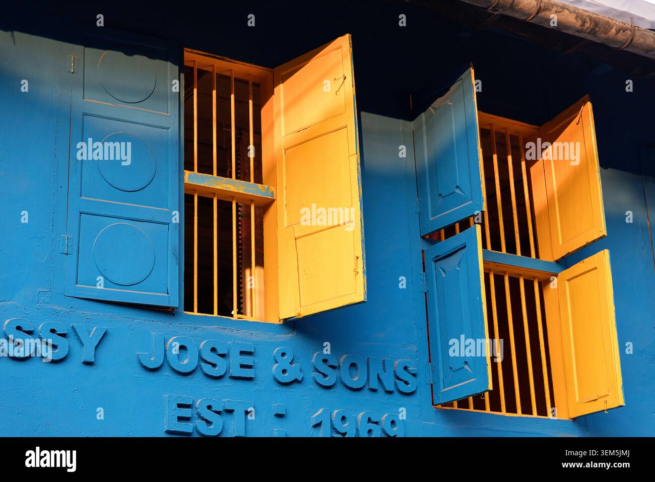 Une vue en angle bas de volets de fenêtre en bois jaune vif s'ouvre contre un mur bleu vif sur un bâtiment du patrimoine à Kochi, Kerala, Inde Banque D'Images