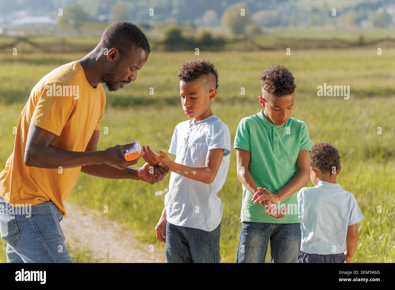 Père applique de la crème solaire à ses enfants par une journée ensoleillée à l'extérieur. La famille profite du temps dans la nature tout en restant en sécurité. Banque D'Images