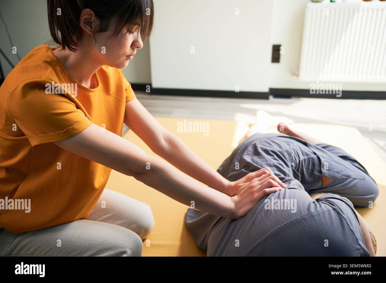Masseuse faisant massage yoga thaïlandais. Femme thérapeute faisant le traitement de massage traditionnel pour le patient masculin à l'intérieur. Client allongé sur tapis, méditant, profitant d'un massage des mains dans une atmosphère calme. Banque D'Images