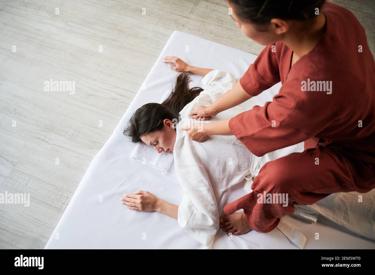 Masseuse faisant massage yoga thaïlandais. Thérapeute de femme faisant le traitement de massage traditionnel pour la patiente féminine à l'intérieur. Client allongé sur tapis, méditant, profitant d'un massage des mains dans une atmosphère calme. Banque D'Images