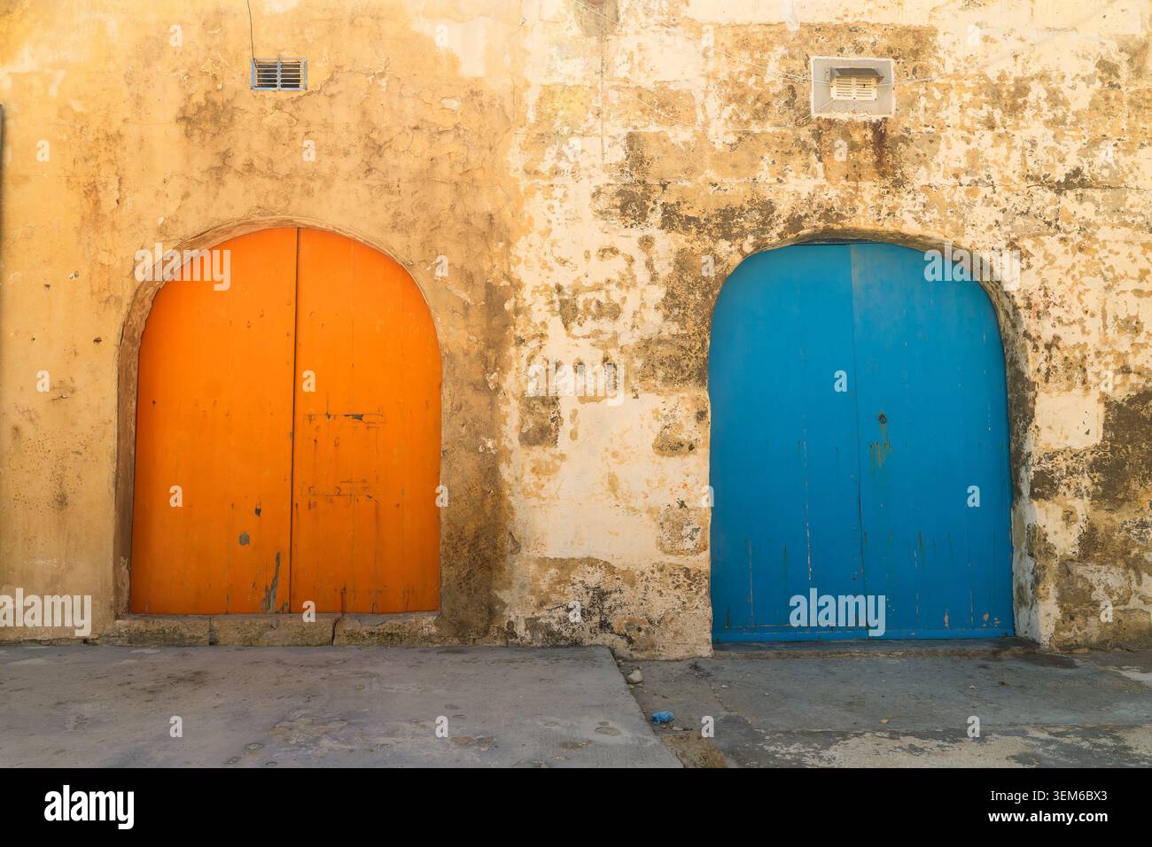 Vue de deux portes en bois cintrées, une orange et une bleue, situées dans un mur de calcaire altéré à Zebbug, région de Gozo, Malte. Banque D'Images