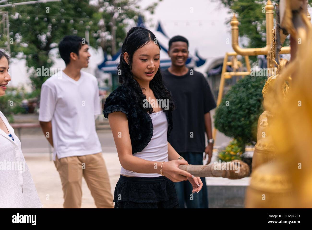 Jeune femme asiatique sonnant les cloches dorées du temple, expérimentant la spiritualité thaïlandaise avec des amis Banque D'Images