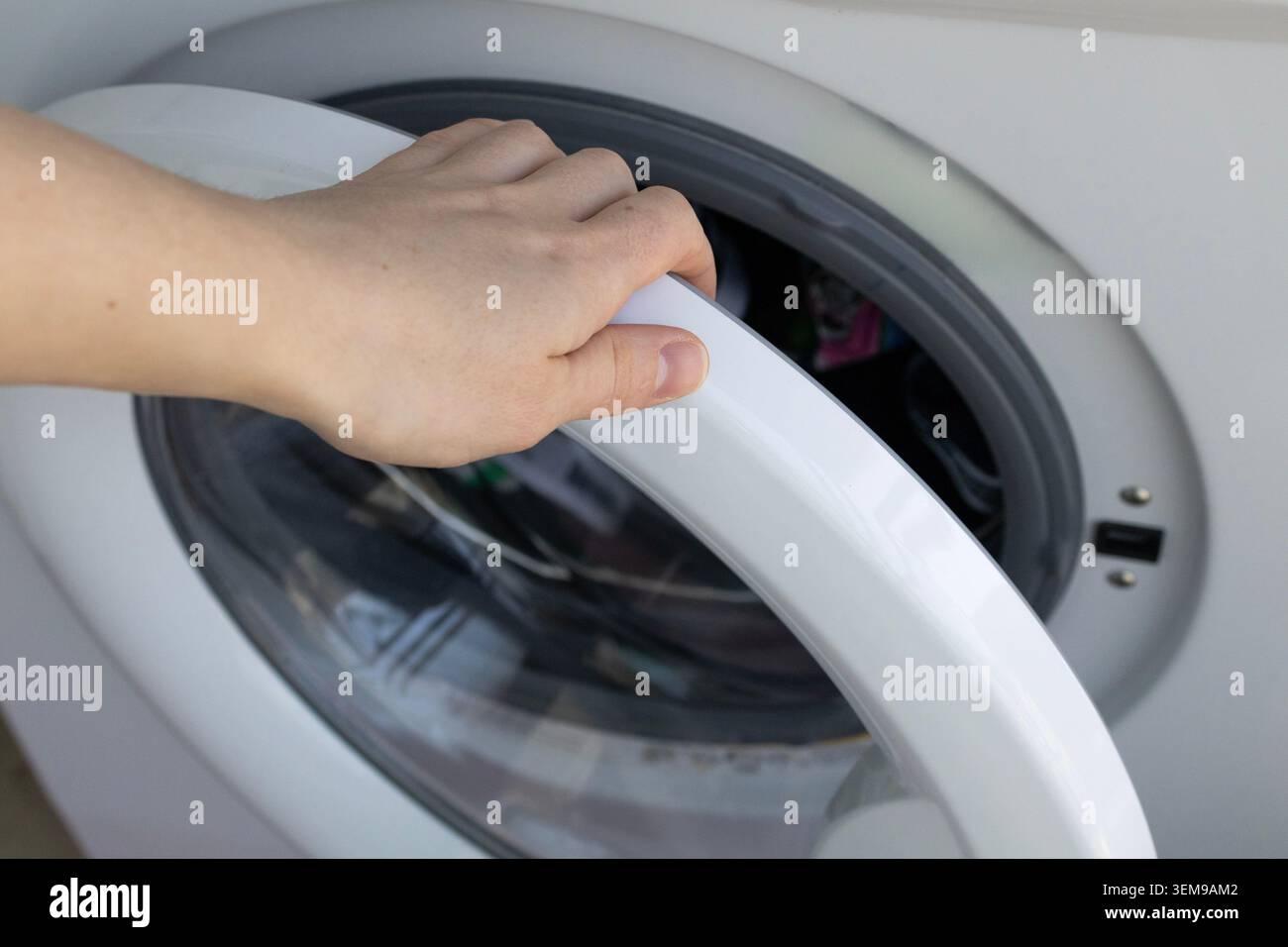Ouverture de la porte du lave-linge à la main avant le cycle de lavage à la maison Banque D'Images