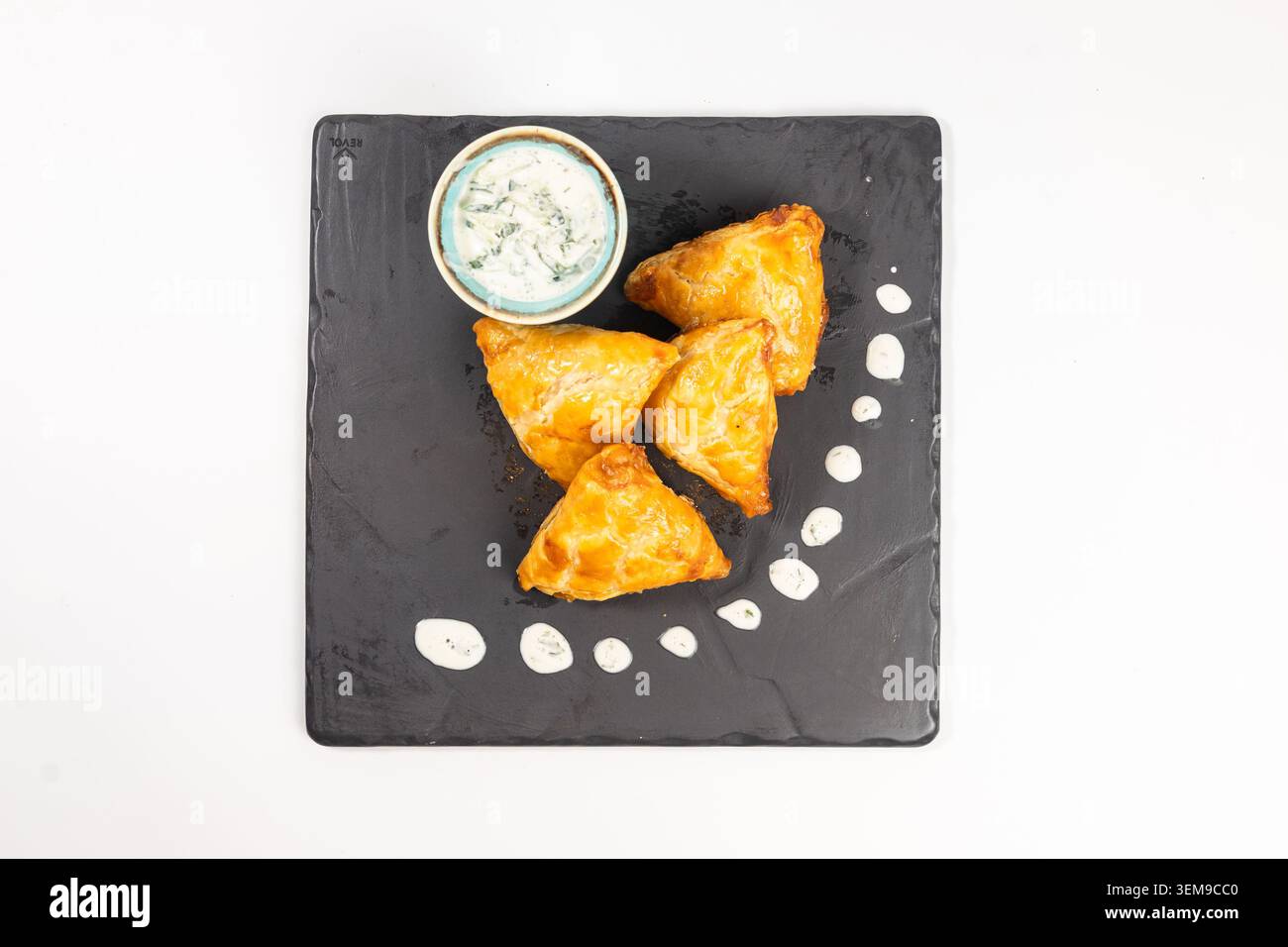 Pâtisseries salées triangulaires traditionnelles servies sur un plateau en pierre sombre avec une sauce aux herbes crème capturée depuis une vue à plat Banque D'Images
