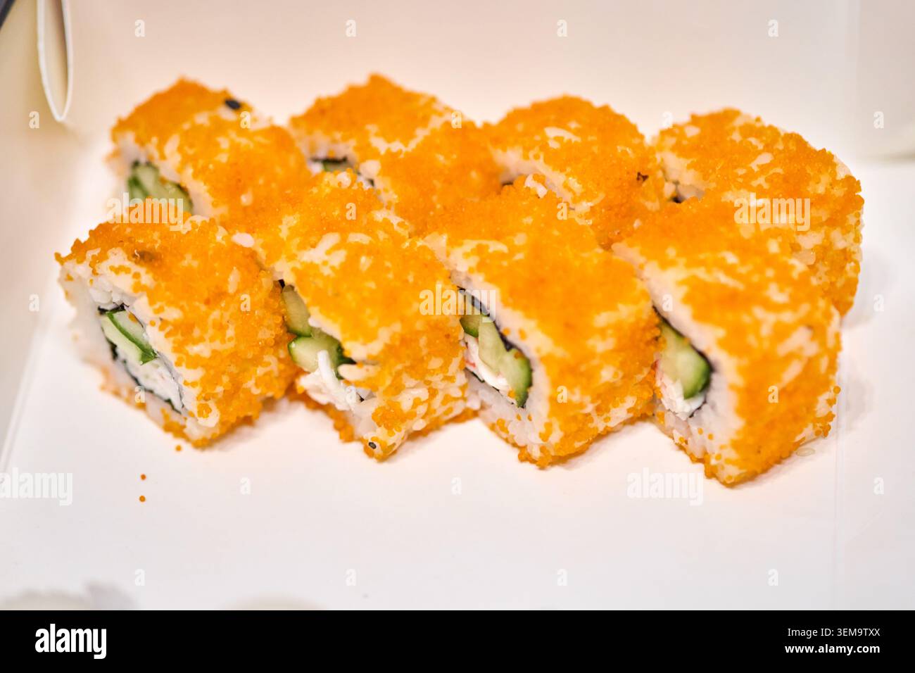 Huit morceaux de rouleaux de sushi makizushi enduits d'œufs de poisson orange vif remplis de concombre et de fromage à la crème sont disposés soigneusement sur la surface blanche un Banque D'Images