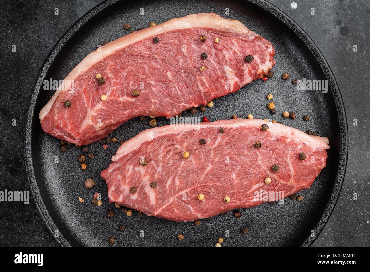 Steaks de bœuf picanha crus également connus sous le nom de chapeau de sirlonge supérieur et de chapeau de croupe avec romarin et poivre sur plaque noire, fond de pierre sombre Banque D'Images