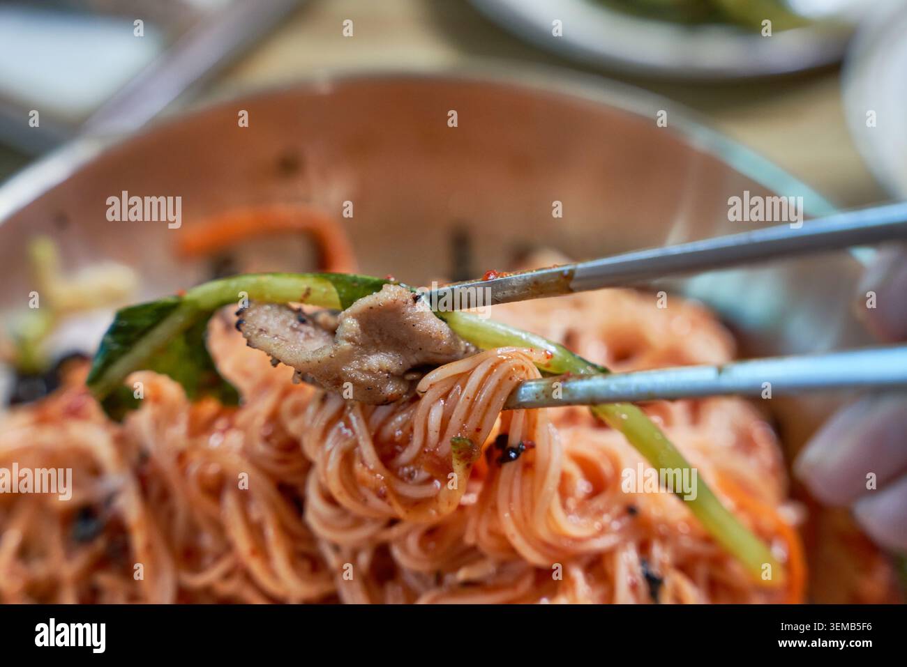 Chapelets de blé froid avec sauce au Chili rouge dans un bol en laiton, accompagnés de bœuf mariné grillé et de kimchi de radis sur une table en bois. Banque D'Images