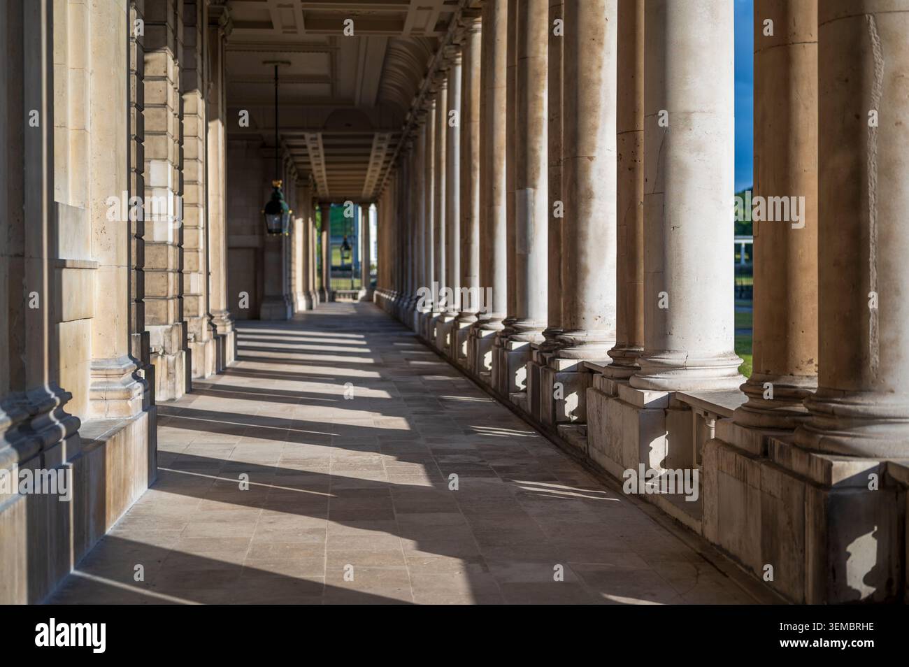 Une vue en perspective d'un seul point donnant sur une grande passerelle couverte ensoleillée bordée d'énormes colonnes de pierre projetant de profondes ombres. Banque D'Images