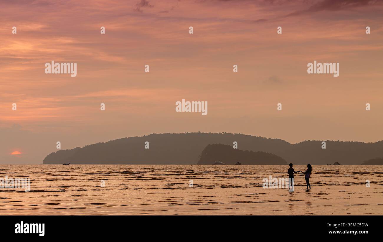 Couple aime se promener au coucher du soleil le long de la plage, créant de beaux souvenirs au bord de la rive. Banque D'Images