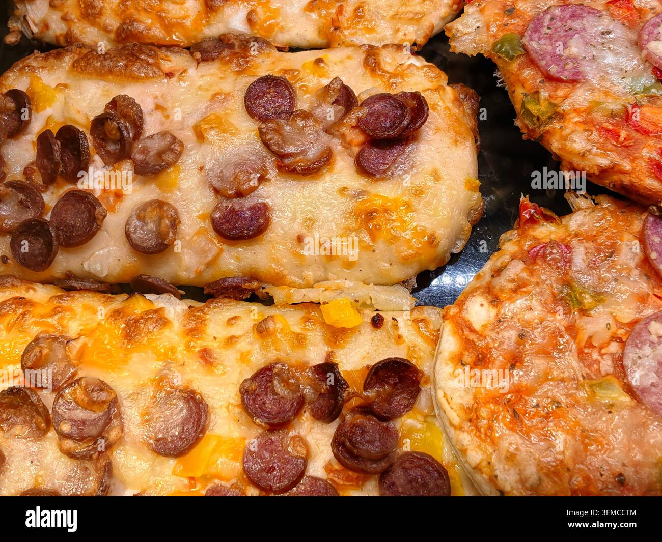 La vue macro montre plusieurs tranches de pizza cuites regroupées sur un plateau sombre. Le fromage fondu recouvre la pâte, les ronds de pepperoni bruns parsèment la surface et Smal Banque D'Images