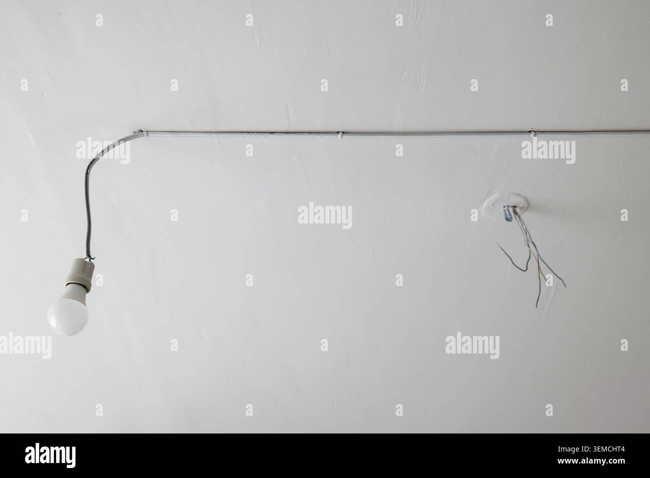 Câblage électrique exposé et ampoule sur plafond blanc Banque D'Images