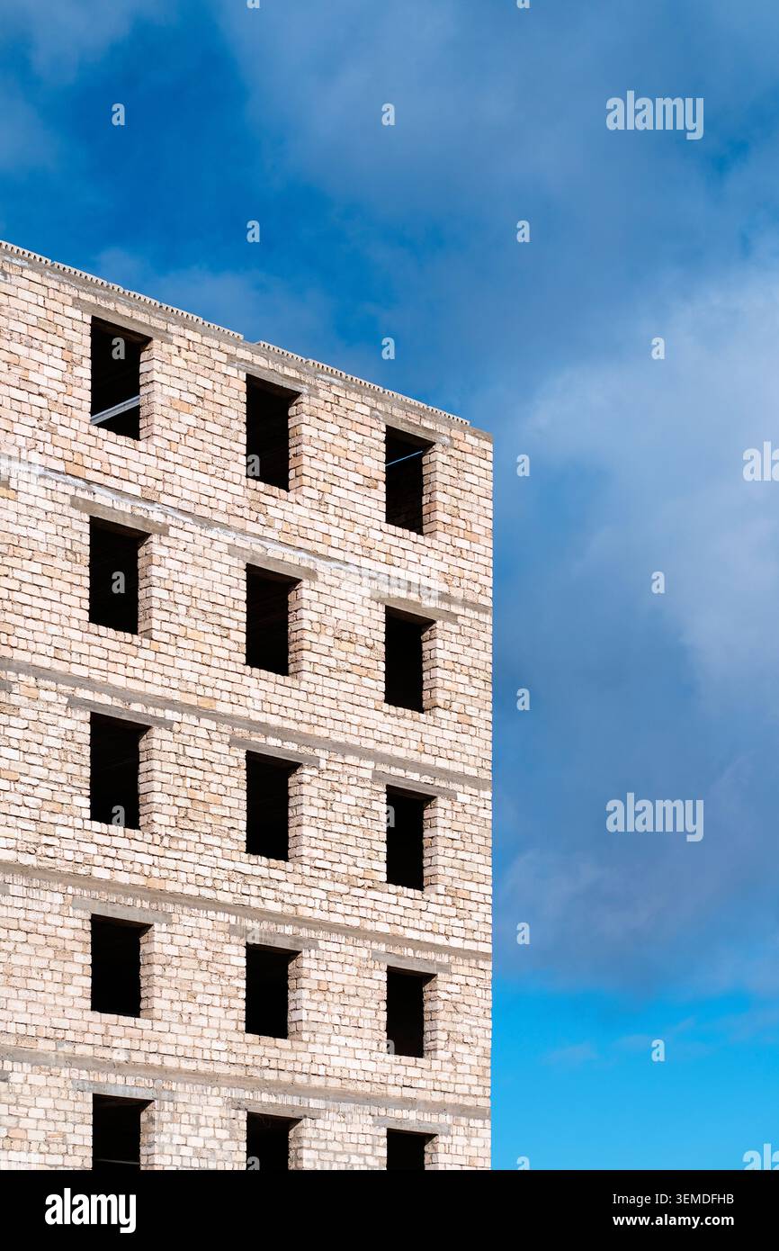 Bâtiment en briques à plusieurs étages inachevé avec des ouvertures de fenêtres vides, capturé par en-dessous contre un ciel bleu, mettant en valeur l'architecture brute et le développement urbain Banque D'Images