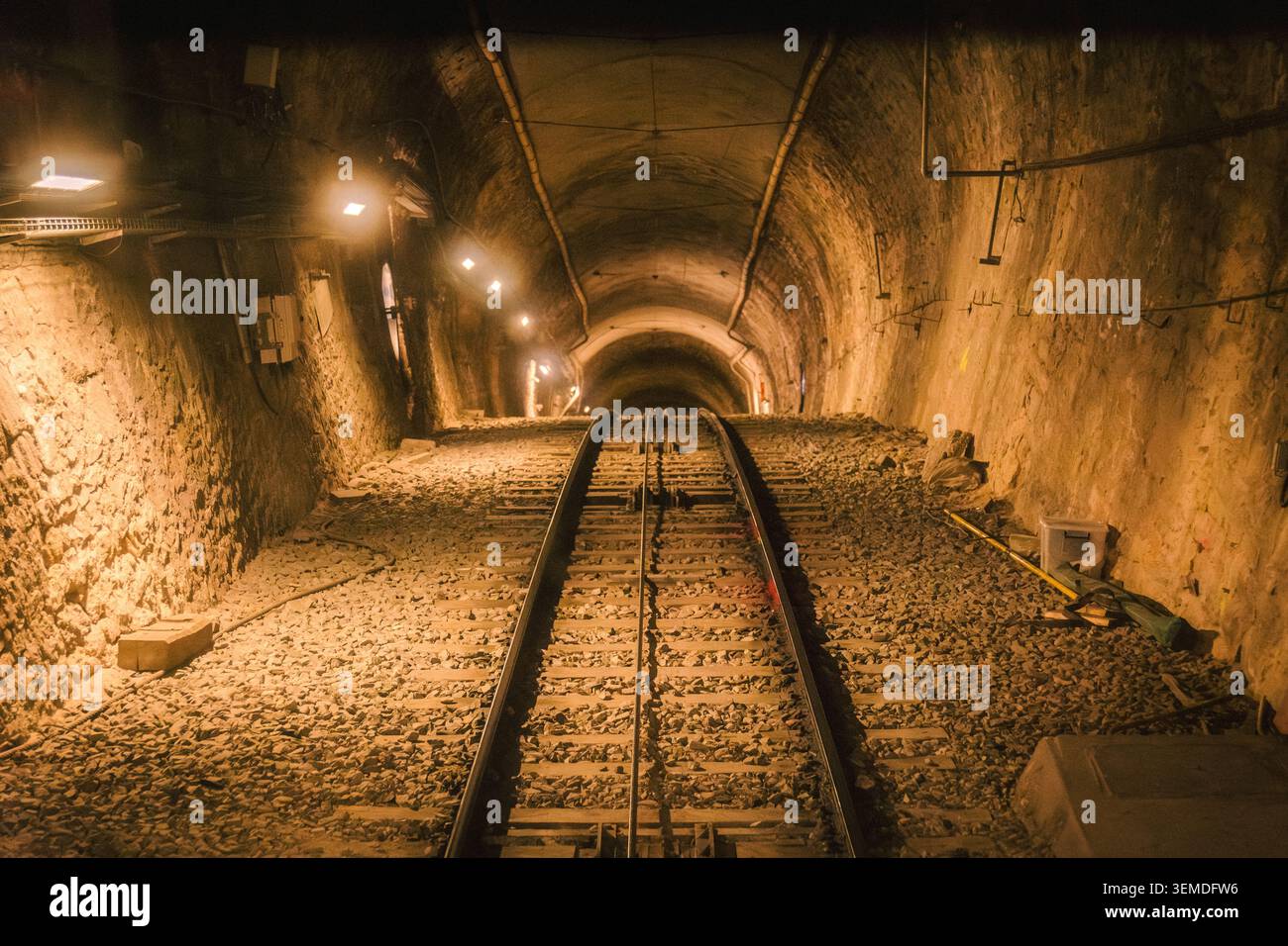 Moody View descend un tunnel ferroviaire souterrain à Lyon, France, avec deux voies, ballast de gravier et éclairage industriel chaleureux créant un transi urbain Banque D'Images