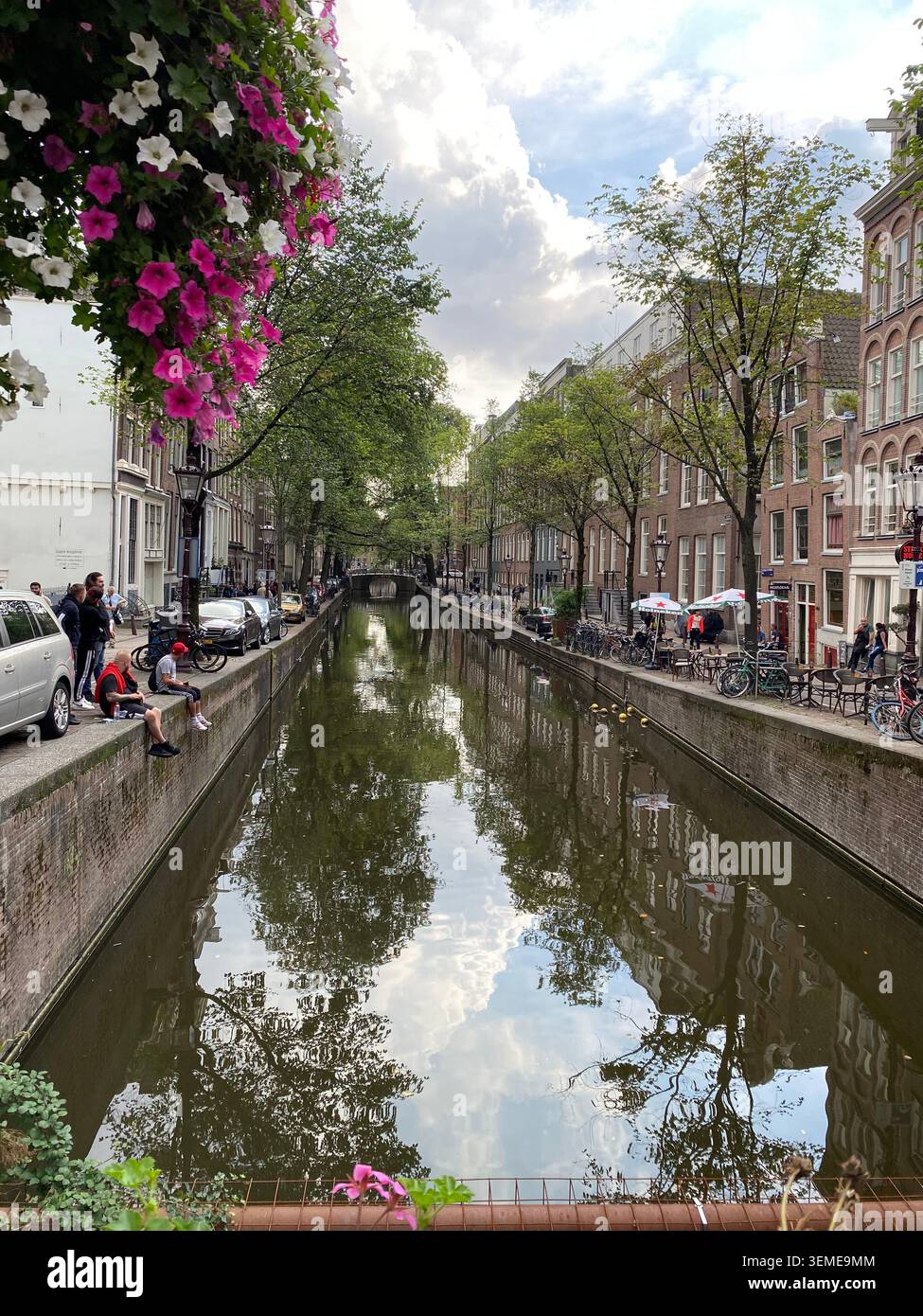 Canal Oudezijds Achterburgwal à Amsterdam, pays-Bas, avec des maisons de canal historiques, des reflets et des fleurs. - Image de stock capturée avec un smartphone
