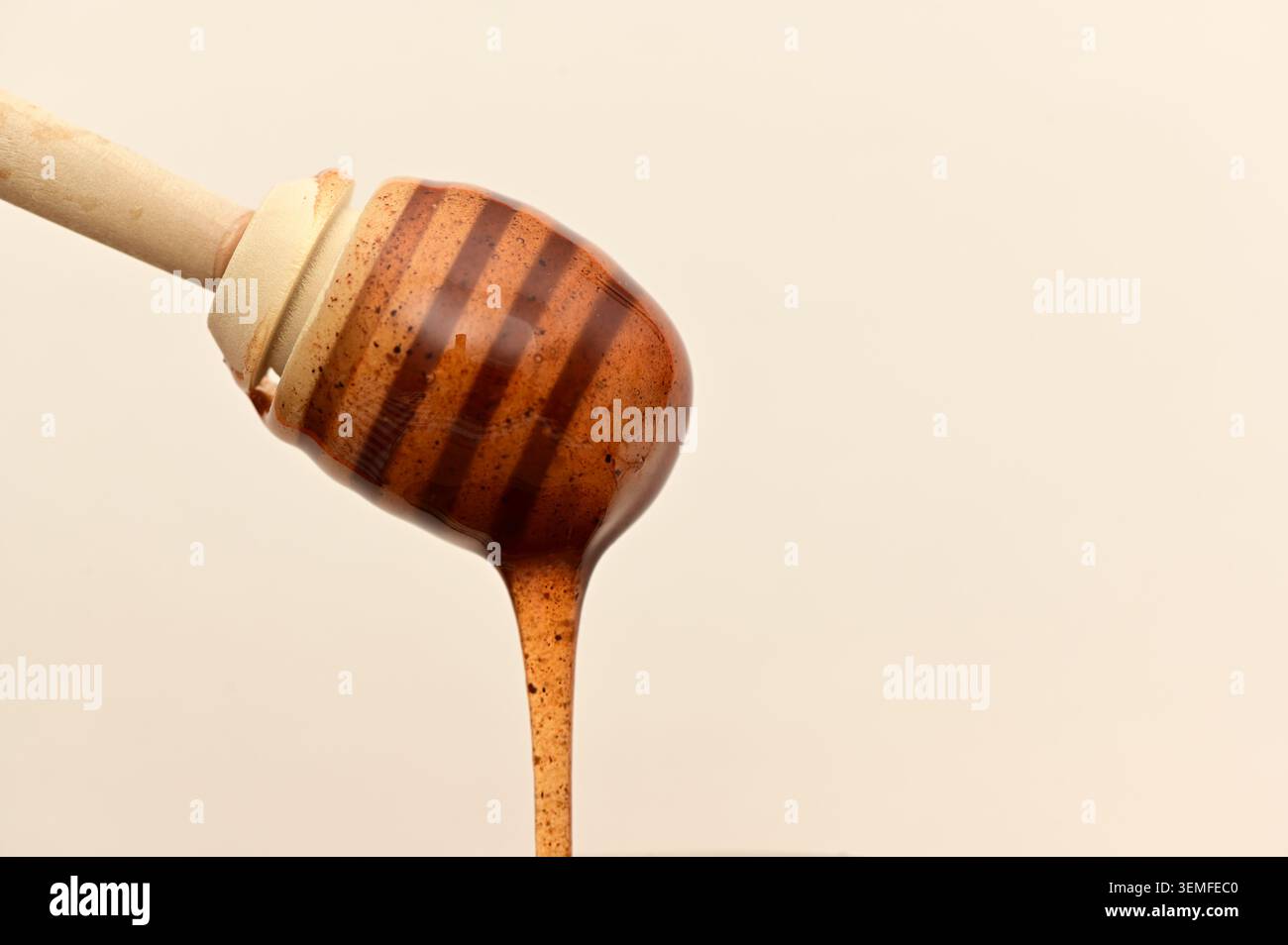 Close-up d'un cuillère en bois à miel avec du miel épais dégoulinant sur un fond beige neutre. Banque D'Images