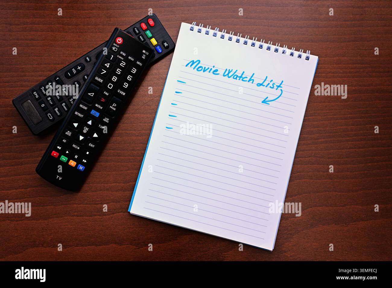 Ordinateur portable en spirale avec « liste de visionnage de films » et deux télécommandes sur une table en bois : planification d'une liste de visionnage, diffusion en continu et concept de divertissement. Banque D'Images