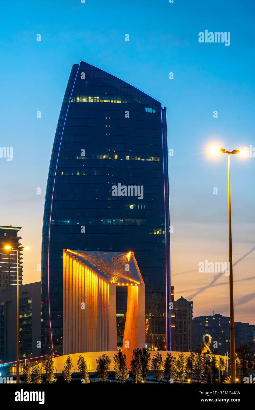 L'arc de triomphe illuminé de Victory Park au premier plan avec Port Baku Tower 2 (Chapman Taylor, 2023) s'élevant derrière au crépuscule. Bakou, Arizona Banque D'Images