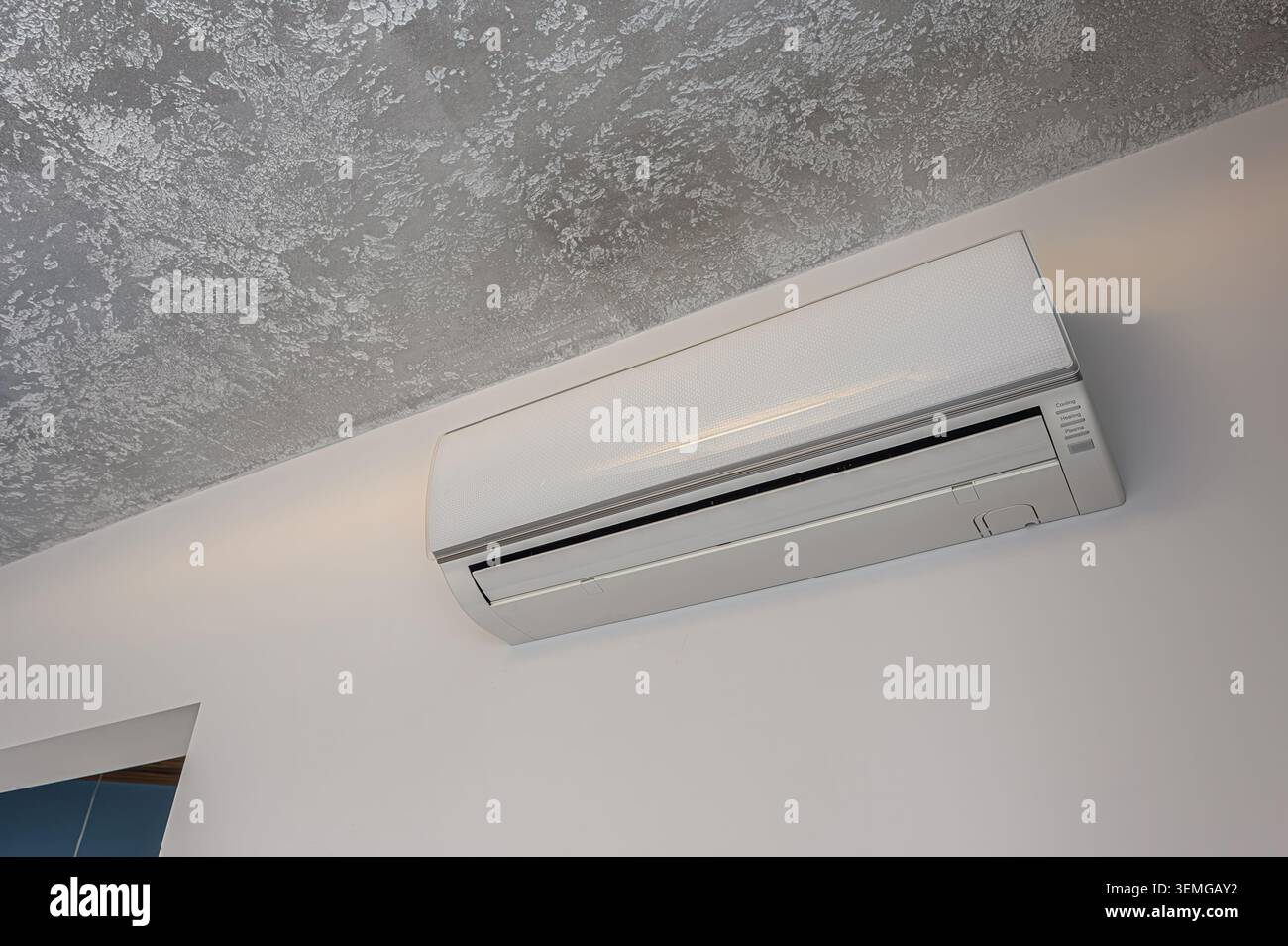 le climatiseur blanc est monté sur un mur blanc sous un plafond gris texturé. Esthétique minimaliste et moderne Banque D'Images