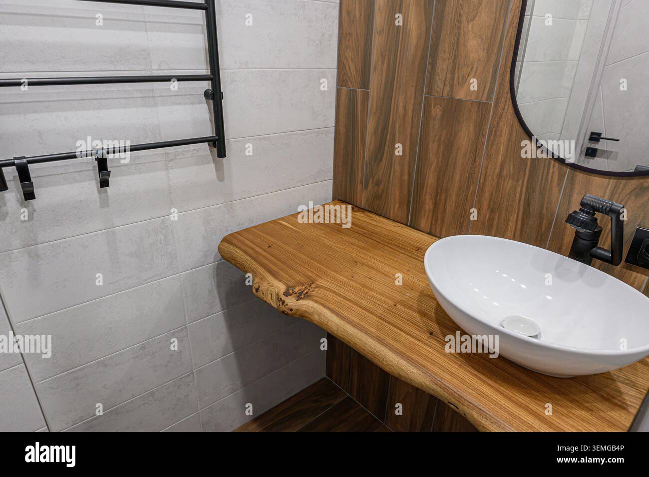 coin salle de bains élégant doté d'un comptoir en bois avec évier ovale blanc, de luminaires noirs et de murs carrelés aux textures gris clair et bois Banque D'Images