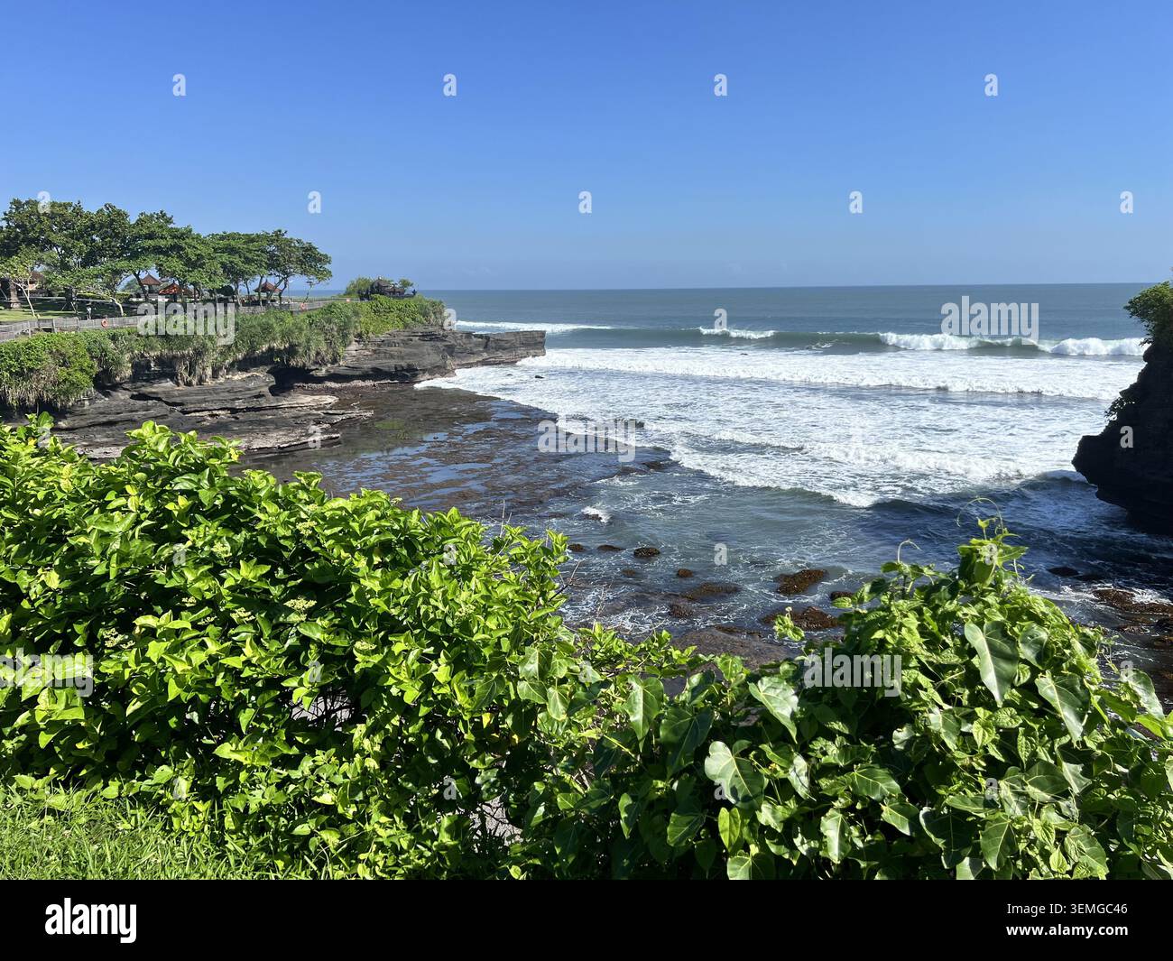 Côte rocheuse avec des vagues écrasantes et une végétation tropicale luxuriante près du complexe du temple Tanah Lot par une journée ensoleillée, Bali, Indonésie. - Image de stock capturée avec un smartphone
