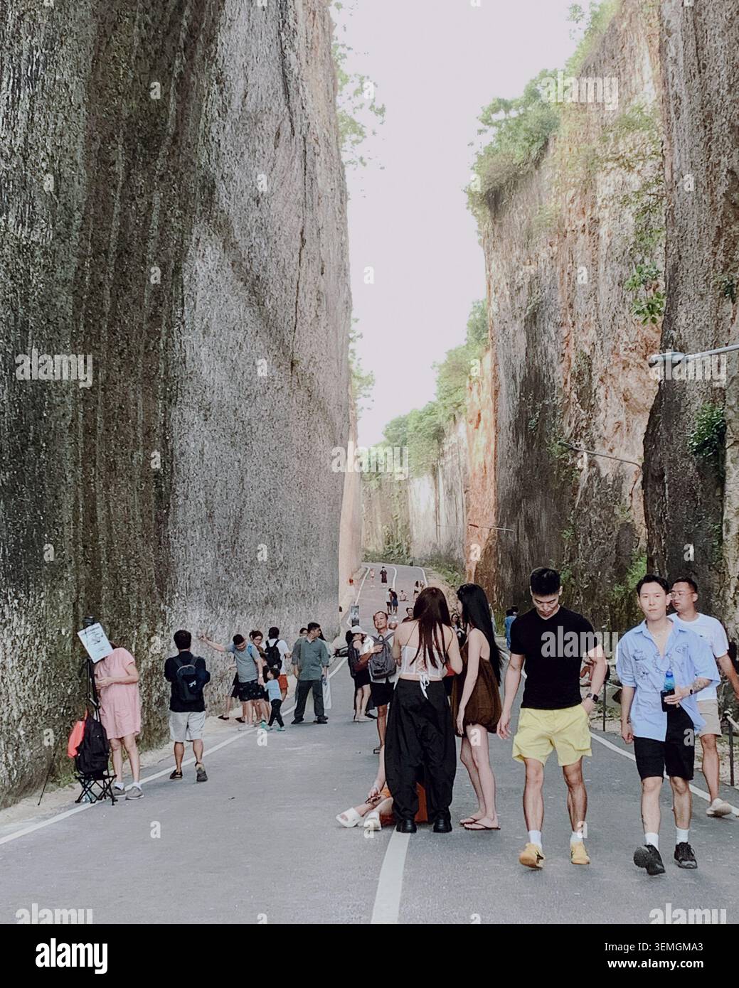 Bali, Indonésie -02 juin 2025 : de hautes falaises encadrent une route sinueuse. Les gens se promènent, discutent ou font une pause, profitant de la vue. Banque D'Images