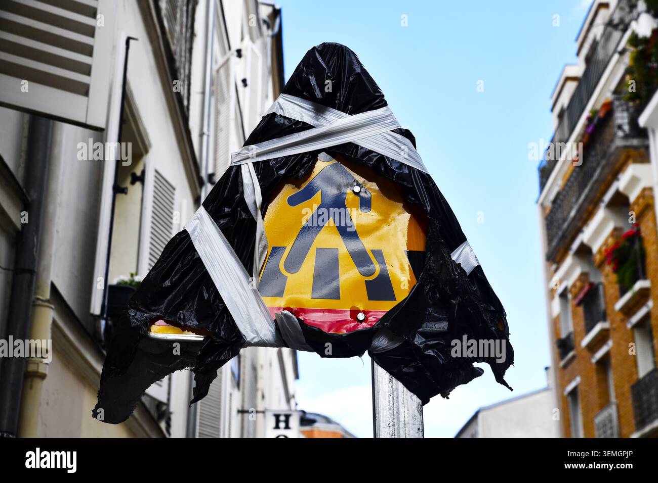 un panneau routier triangulaire jaune pour passage piéton enveloppé et scotché avec un sac en plastique noir et du ruban adhésif blanc sur un poteau métallique dans une rue de ville Banque D'Images