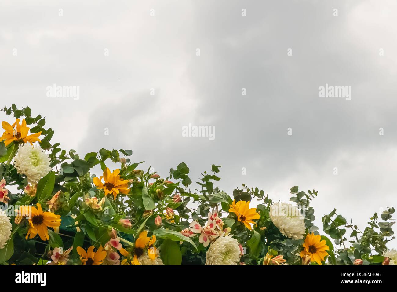 Arrangement floral décoratif avec fleurs jaune vif, chrysanthèmes blancs et feuillage vert sous un ciel couvert dramatique avec de nombreuses copies Banque D'Images