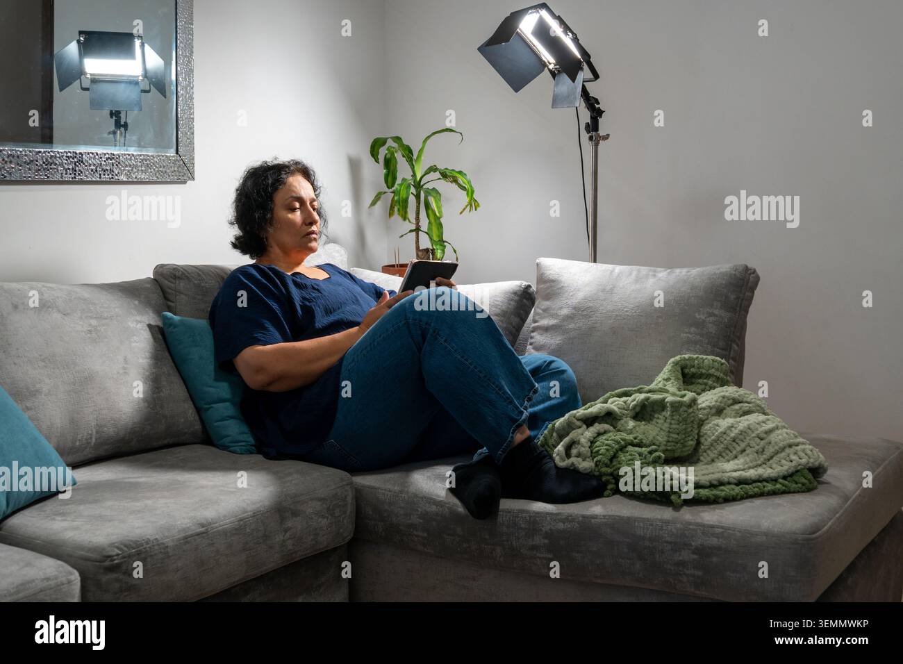 Femme assise sur un canapé lisant un livre numérique, profitant du temps libre à l'intérieur Banque D'Images