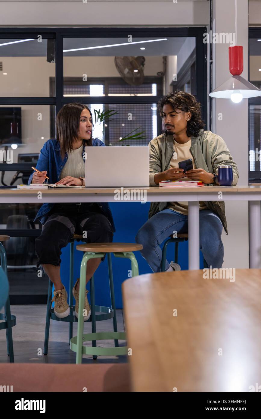 Divers collègues assis à la table commune haute dans l'espace de co-working, prenant des notes avec un ordinateur portable Banque D'Images