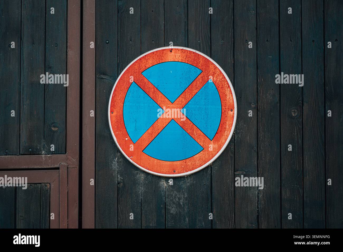 Un panneau de signalisation rond sans stationnement avec une bordure rouge rouillée et un centre bleu vif monté sur un mur en bois foncé, véhiculant une restriction urbaine, a été altéré Banque D'Images