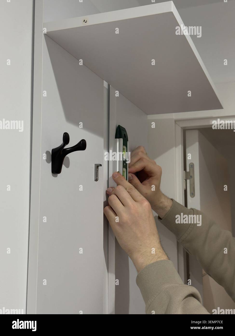 Mains en utilisant un niveau à bulle vert sur le panneau blanc du porte-manteau pendant l'installation du meuble Banque D'Images
