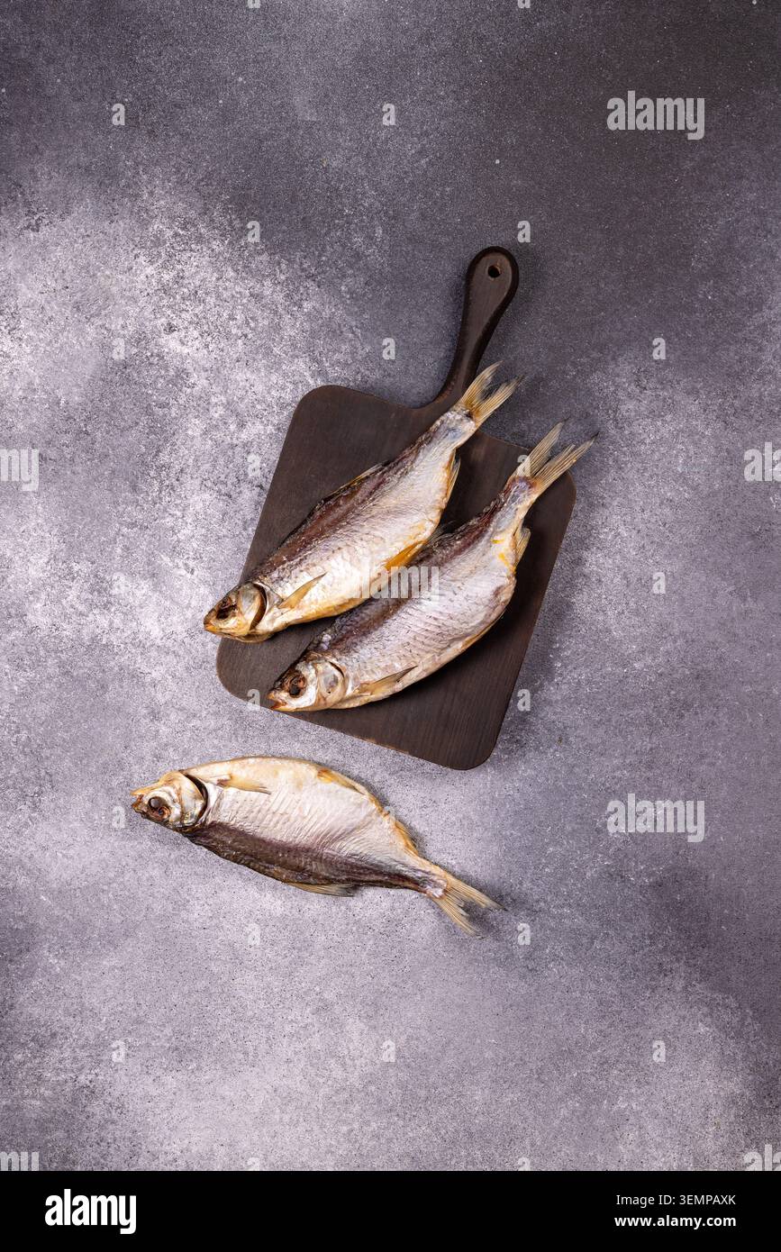 Poisson séché salé, une collation traditionnelle, reposant sur une planche de bois sombre et directement sur un fond gris texturé, symbolisant le prépar alimentaire traditionnel Banque D'Images
